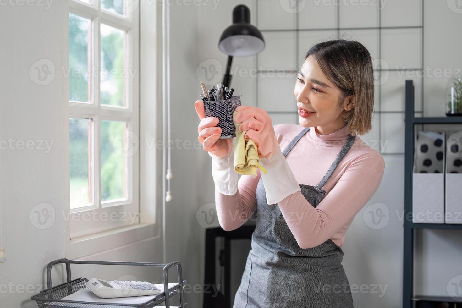 ama de casa limpieza y organizando hogar oficina espacio con un sonrisa, vistiendo delantal y guantes, brillante y moderno interior foto