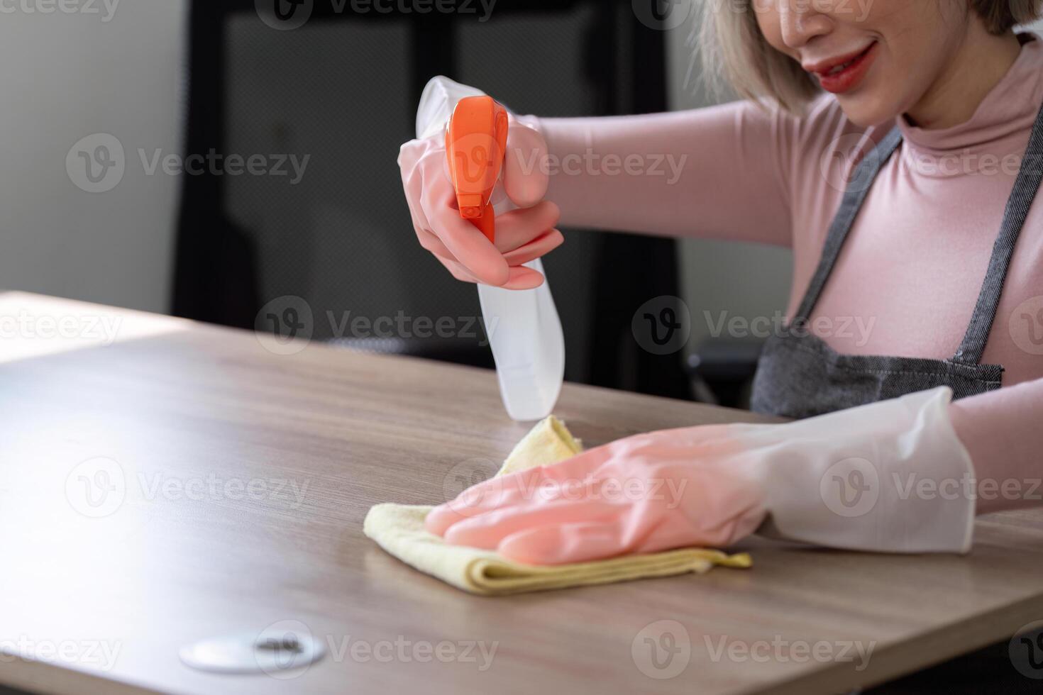 Housekeeper Cleaning a Wooden Table with Spray Bottle and Cloth in Modern Home Environment photo