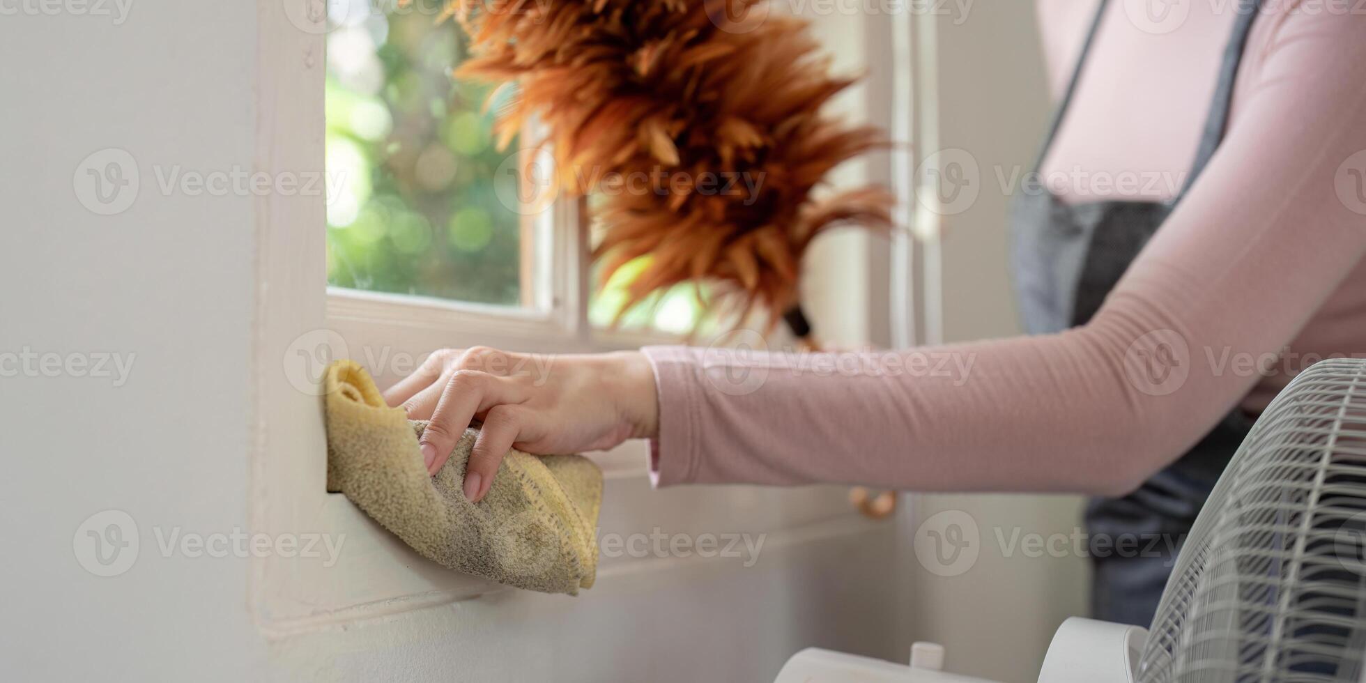 Housekeeper Cleaning Window Sill with Cloth and Feather Duster in Modern Home Interior photo