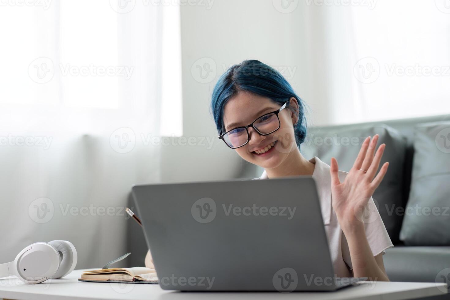 Happy young woman asian using laptop sitting at desk writing notes while watching webinar, studying online, looking at laptop screen learning web classes or having call remote from home photo