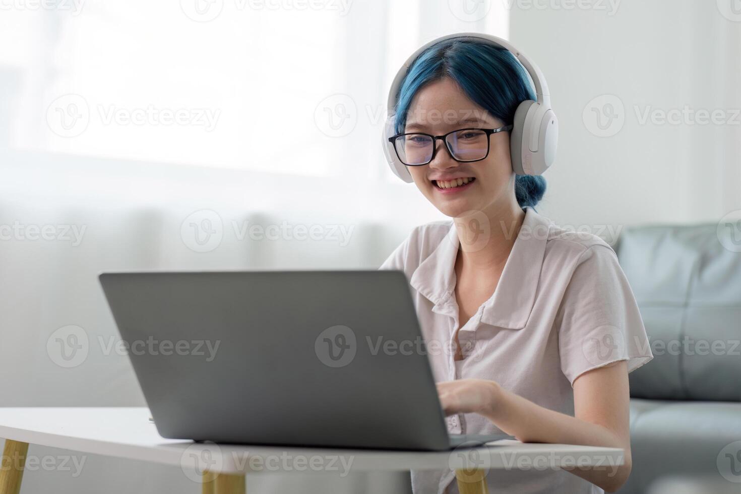 Smiling girl student wear headphone study online with teacher, happy young asian woman learn lecture watch webinar write notes look at laptop sit in home, distant education photo