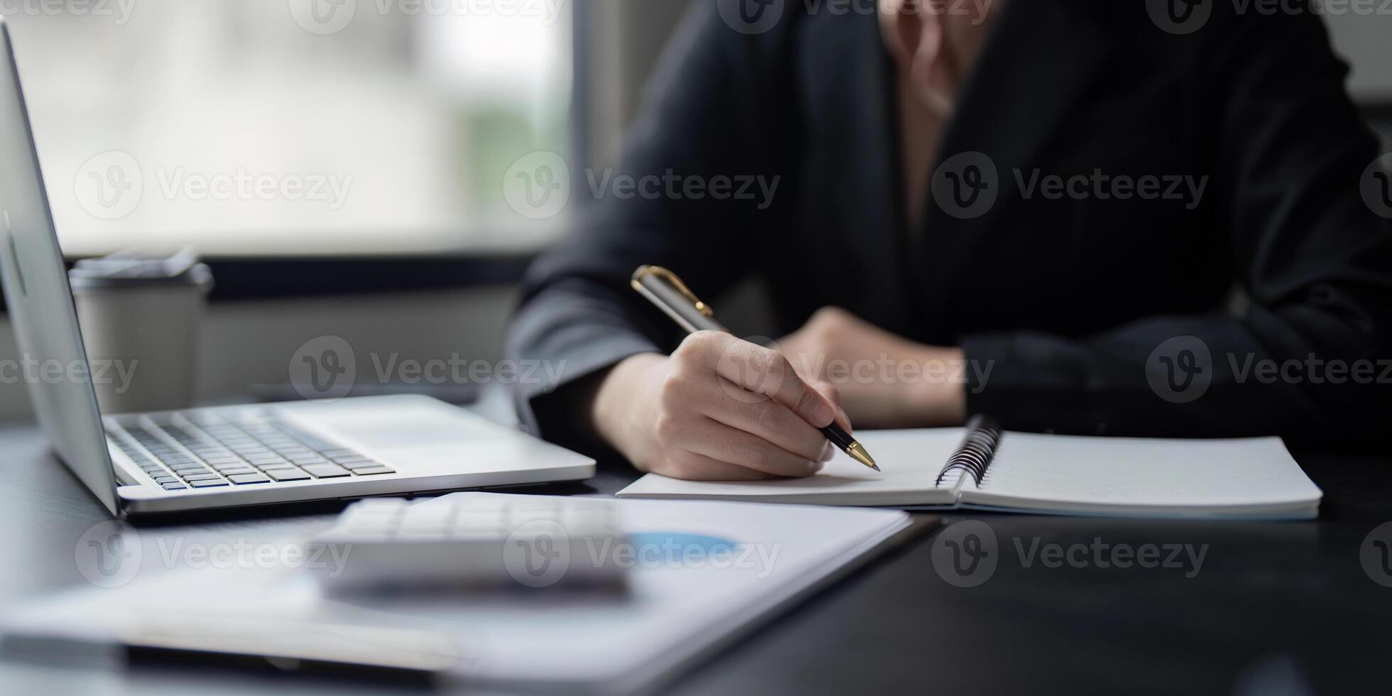 Business Professional Writing Notes at Desk with Laptop and Documents in Modern Office Setting photo