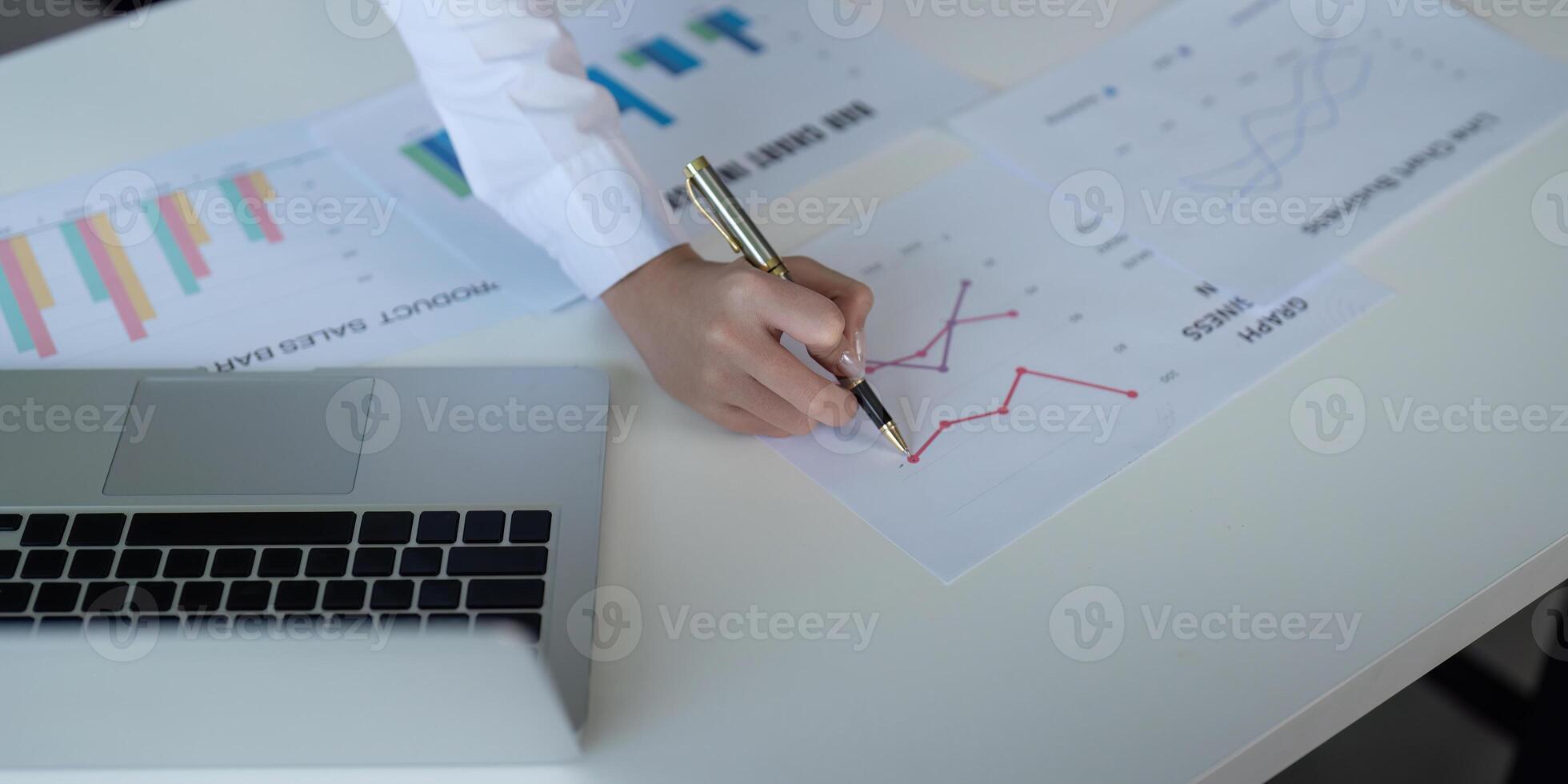 Finance concept. Close up businesswoman hold a graph pen and writing report, and memo, and analyzing business documents with a laptop computer photo