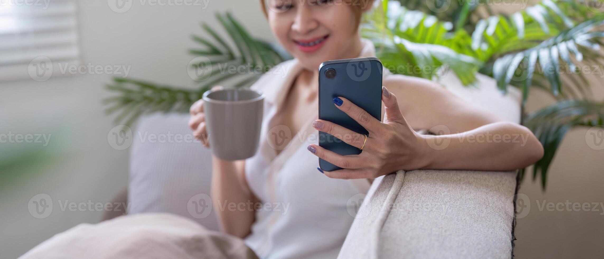 Woman Relaxing at Home Using Smartphone for Social Media While Drinking Coffee in a Cozy Living Room photo