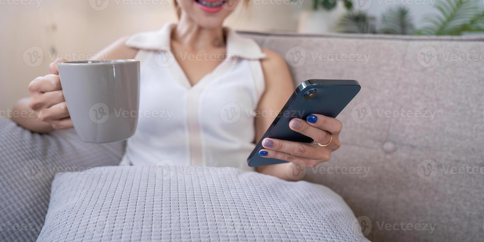 Woman Enjoying Social Media at Home with Coffee, Relax on Sofa, Smiling and Engaged with Smartphone photo
