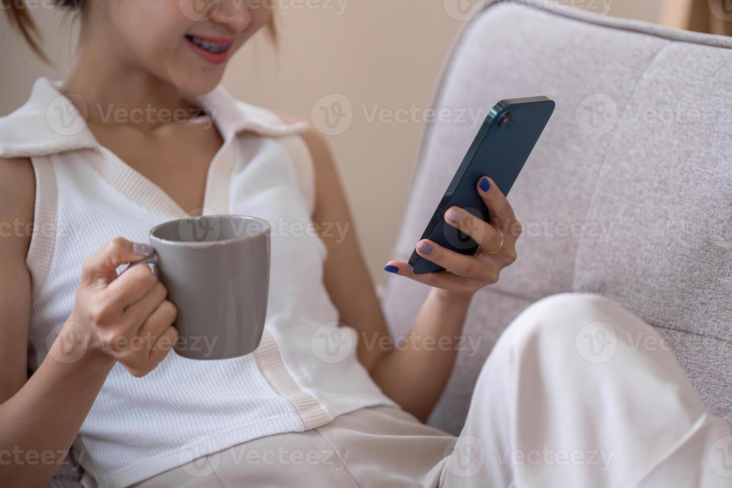 Young Woman Relax on Couch Using Smartphone and Drinking Coffee for Social Media Browsing photo