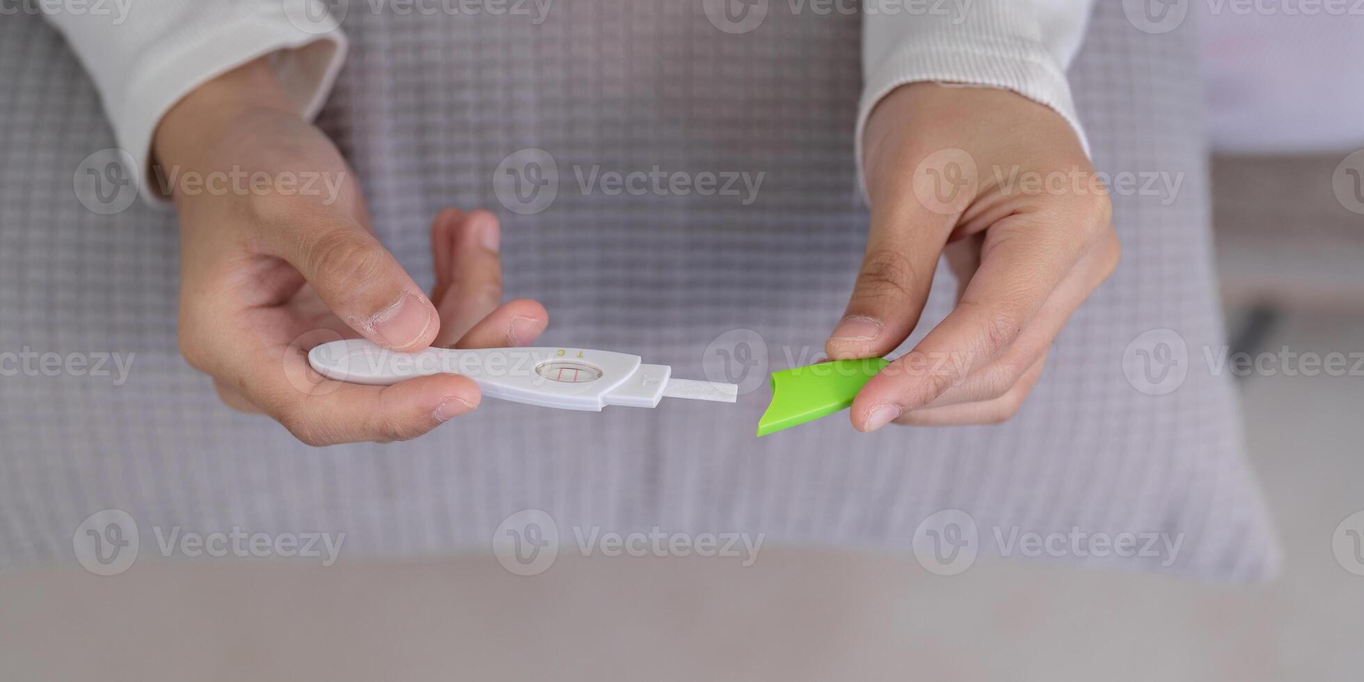 Close up of Hands Holding a Pregnancy Test Kit with a Pillow in the Background, Focus on the Abdomen Area photo