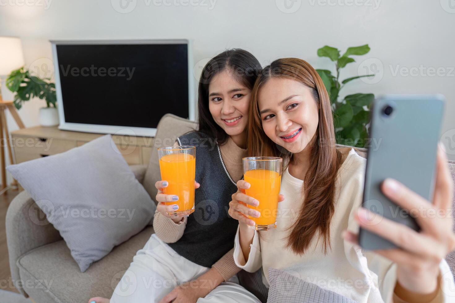 Happy Lesbian Couple Enjoying Healthy Orange Juice While Taking a Selfie at Home photo