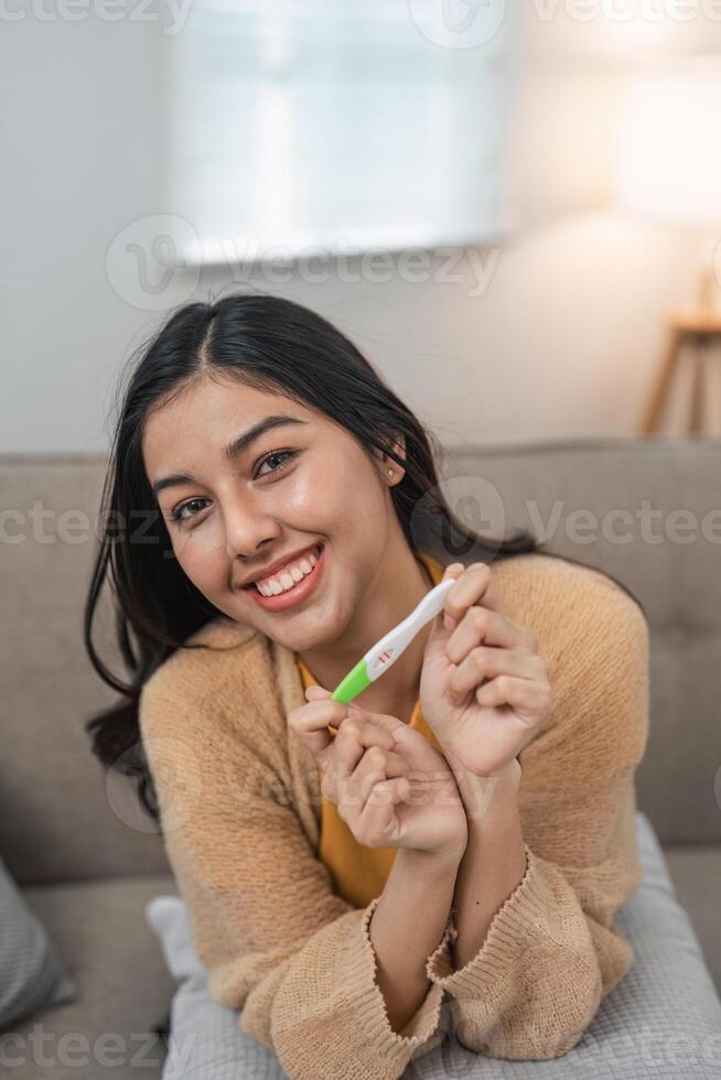 Joyful Woman Holding Positive Pregnancy Test at Home, Celebrating Exciting News with a Bright Smile and Happy Expression photo