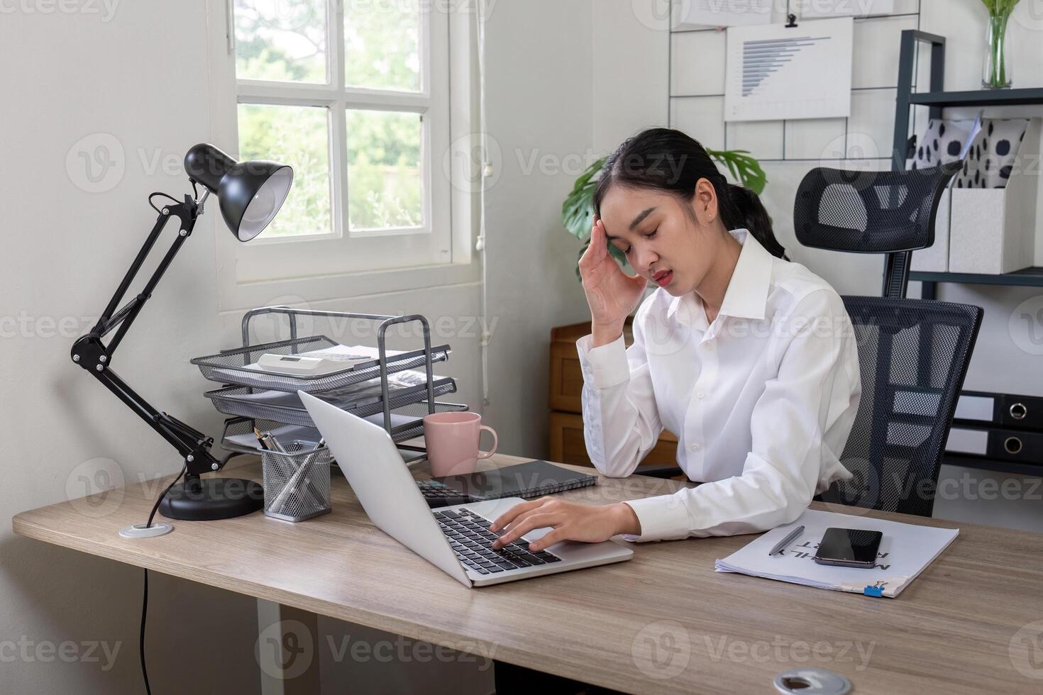 Stress Businesswoman Experiencing Headache at Work Desk with Laptop and Documents in Modern Office Setting photo