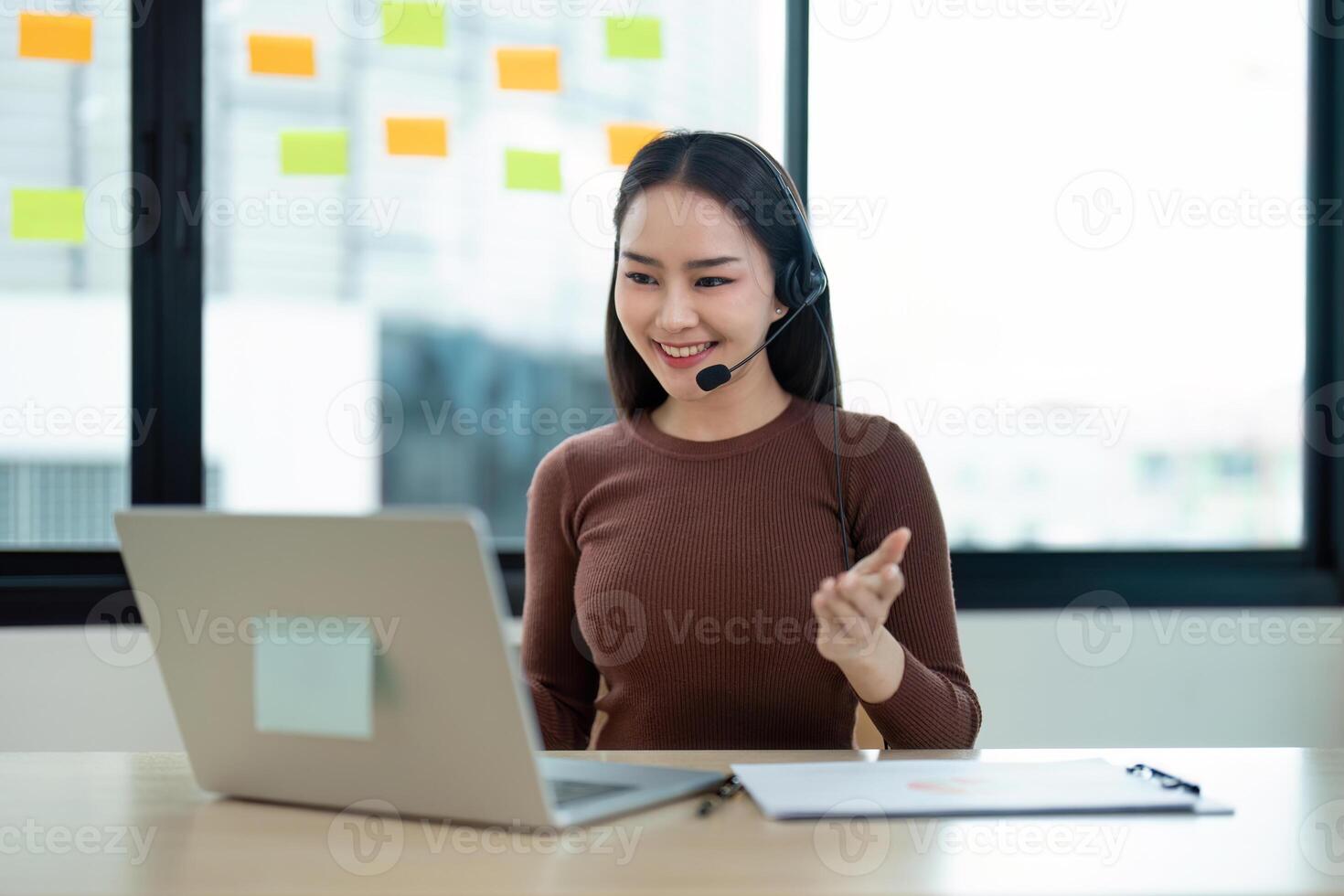 Smiling Call Center Agent with Headset Working on Laptop in Modern Office with Sticky Notes on Glass Wall photo