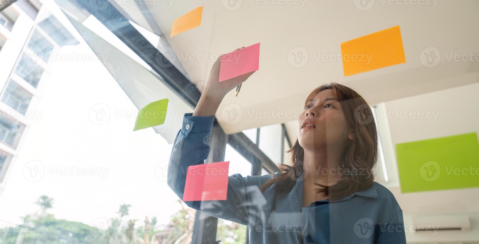 Business Analysis Concept with Sticky Notes. Professional Woman Planning Strategy on Glass Wall in Modern Office photo