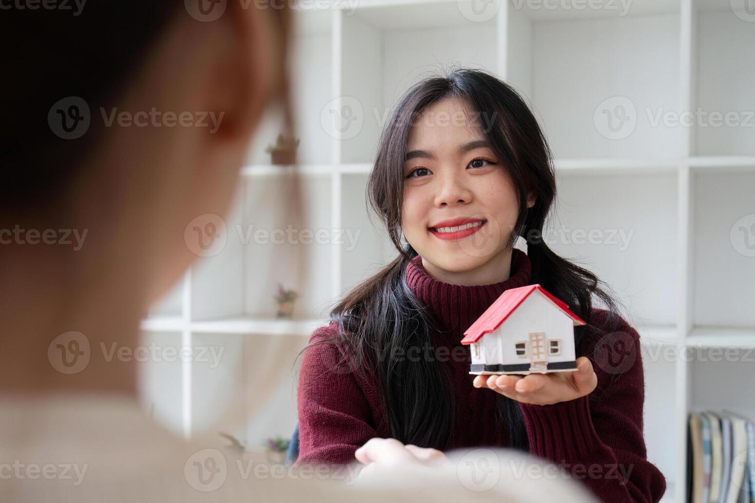 Smiling Real Estate Agent Holding a Model House, Promoting Home Sales or Home Insurance in a Modern Office Setting photo