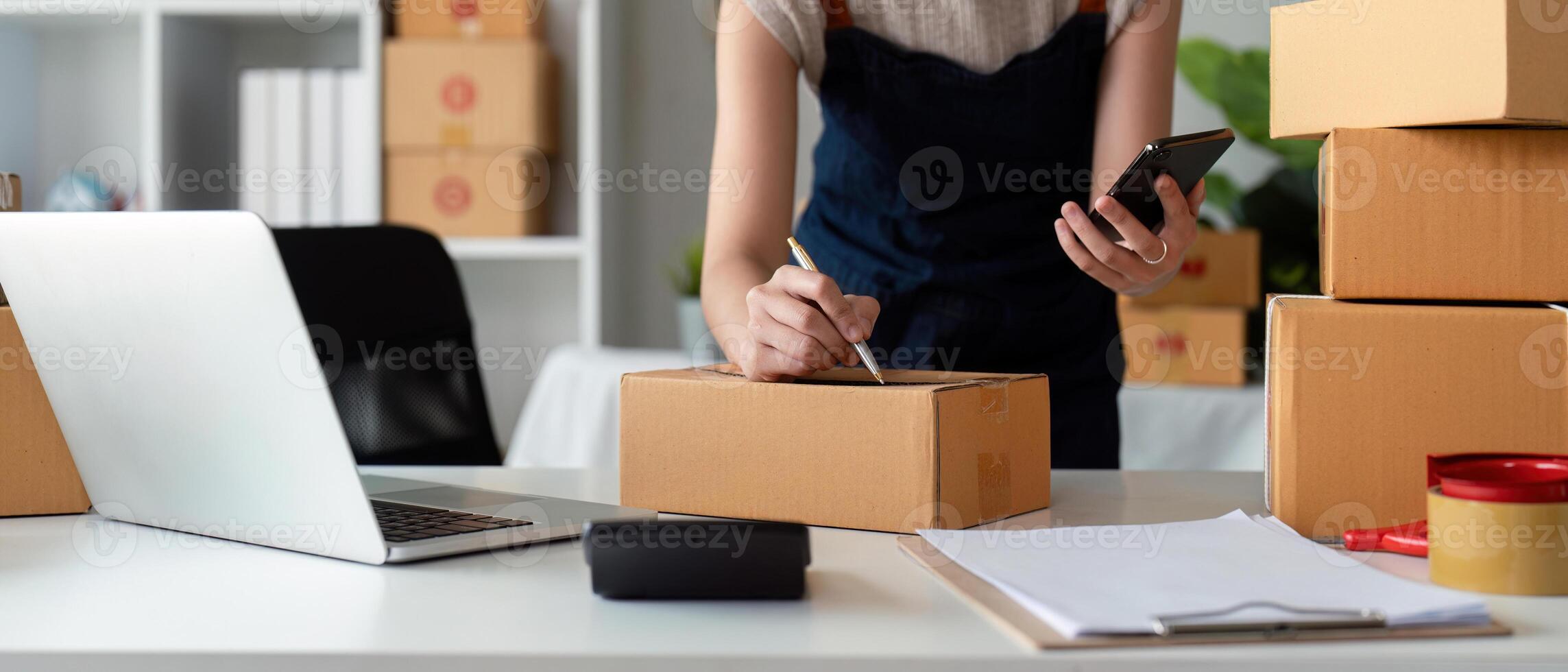 Small Business Owner Preparing Parcel Box for Delivery in Online Ecommerce Store with Laptop and Smartphone photo