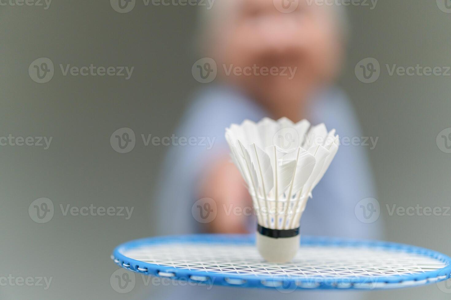 Selective focus of shuttlecock and badminton racket with blurred Asian senior sportswoman in background photo