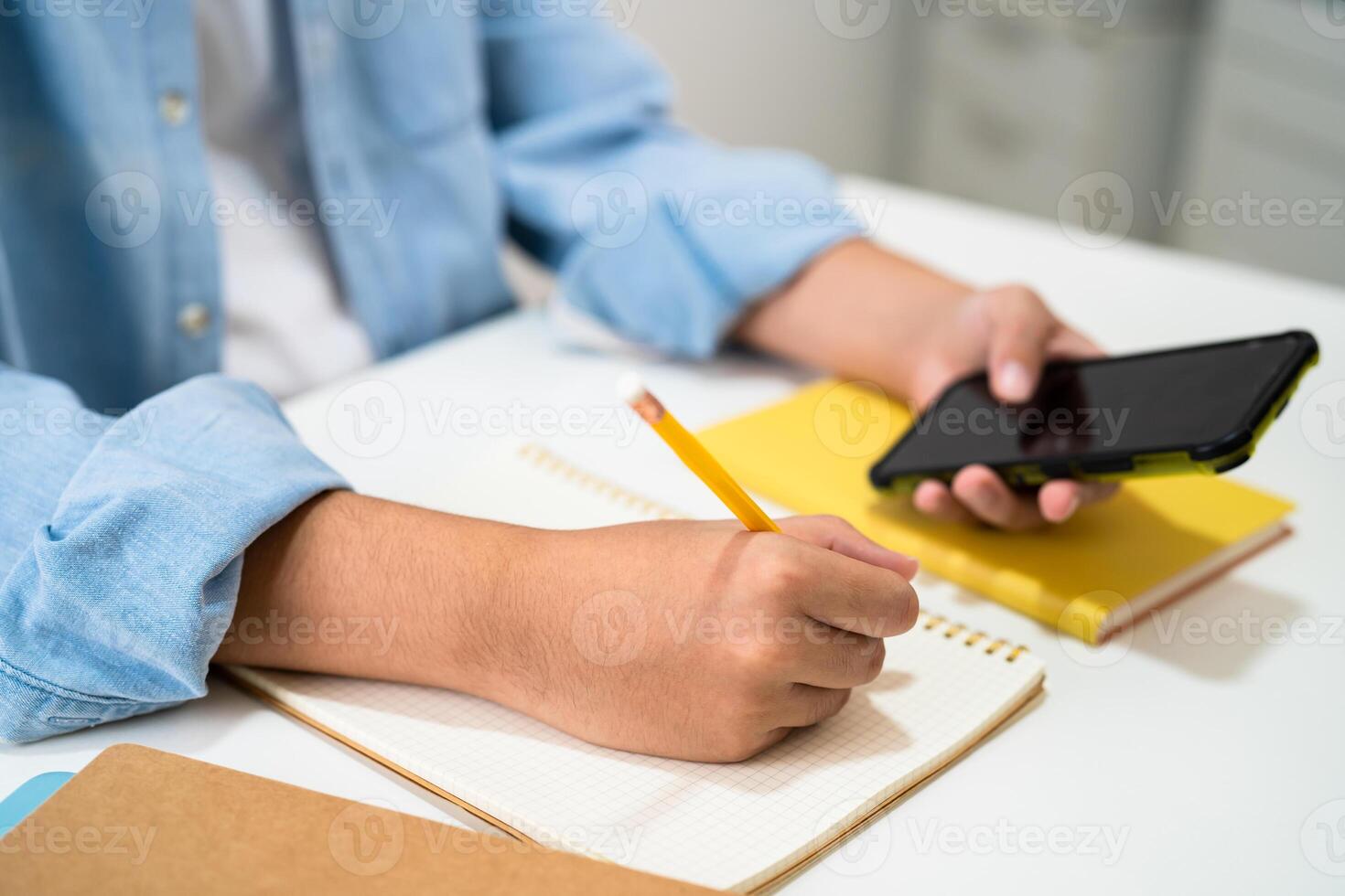 Teenage write in notebook and use mobile phone search data online to online learning university education. photo