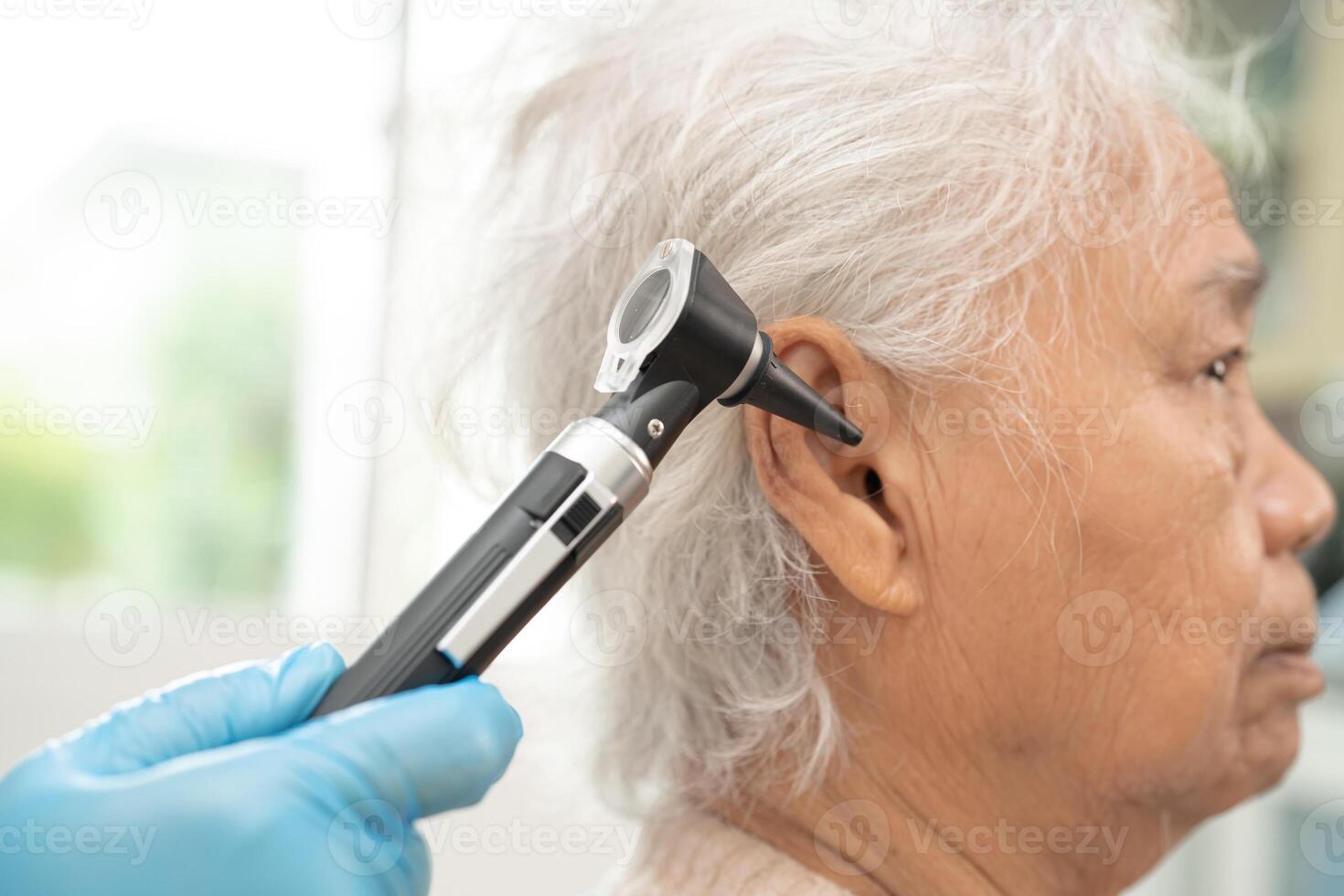 Audiologist or ENT doctor use otoscope checking ear of asian senior woman patient treating hearing loss problem. photo