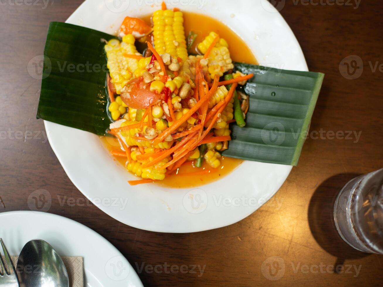 Thai Papaya Salad with Corn serve on banana leaf decoration on plate on wooden table on top view with fork and spoon photo