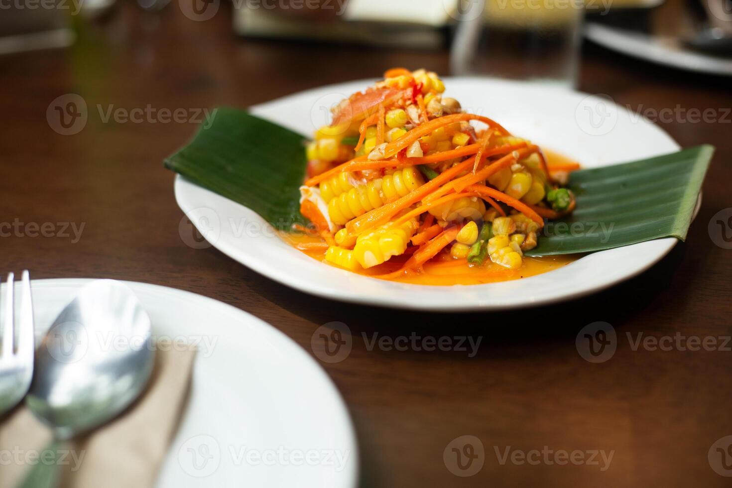 Thai Papaya Salad with Corn serve on banana leaf decoration on plate on wooden table on top view with fork and spoon photo