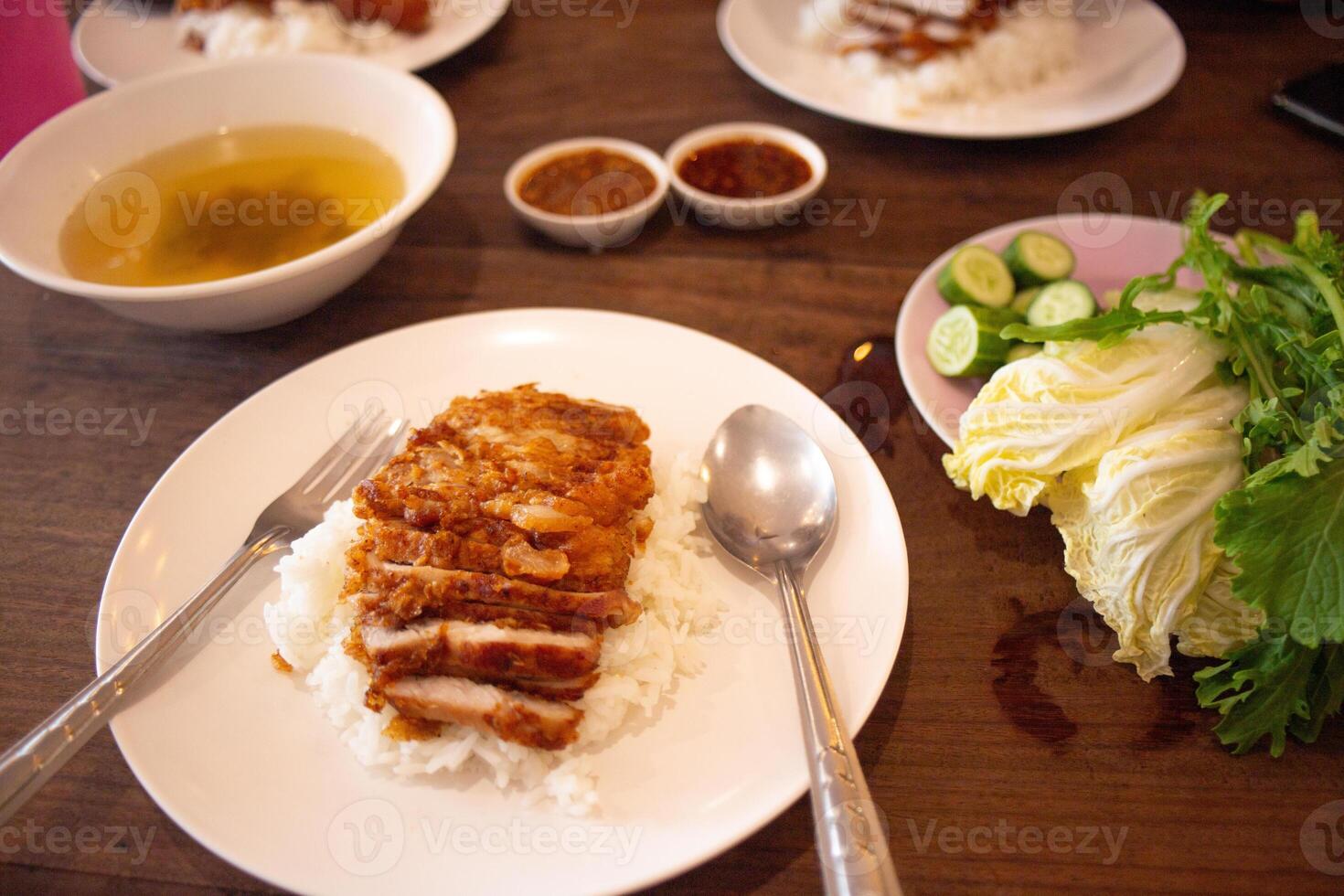 Fried pork with rice, fresh vegetables, chili paste, soup on a wooden table. photo