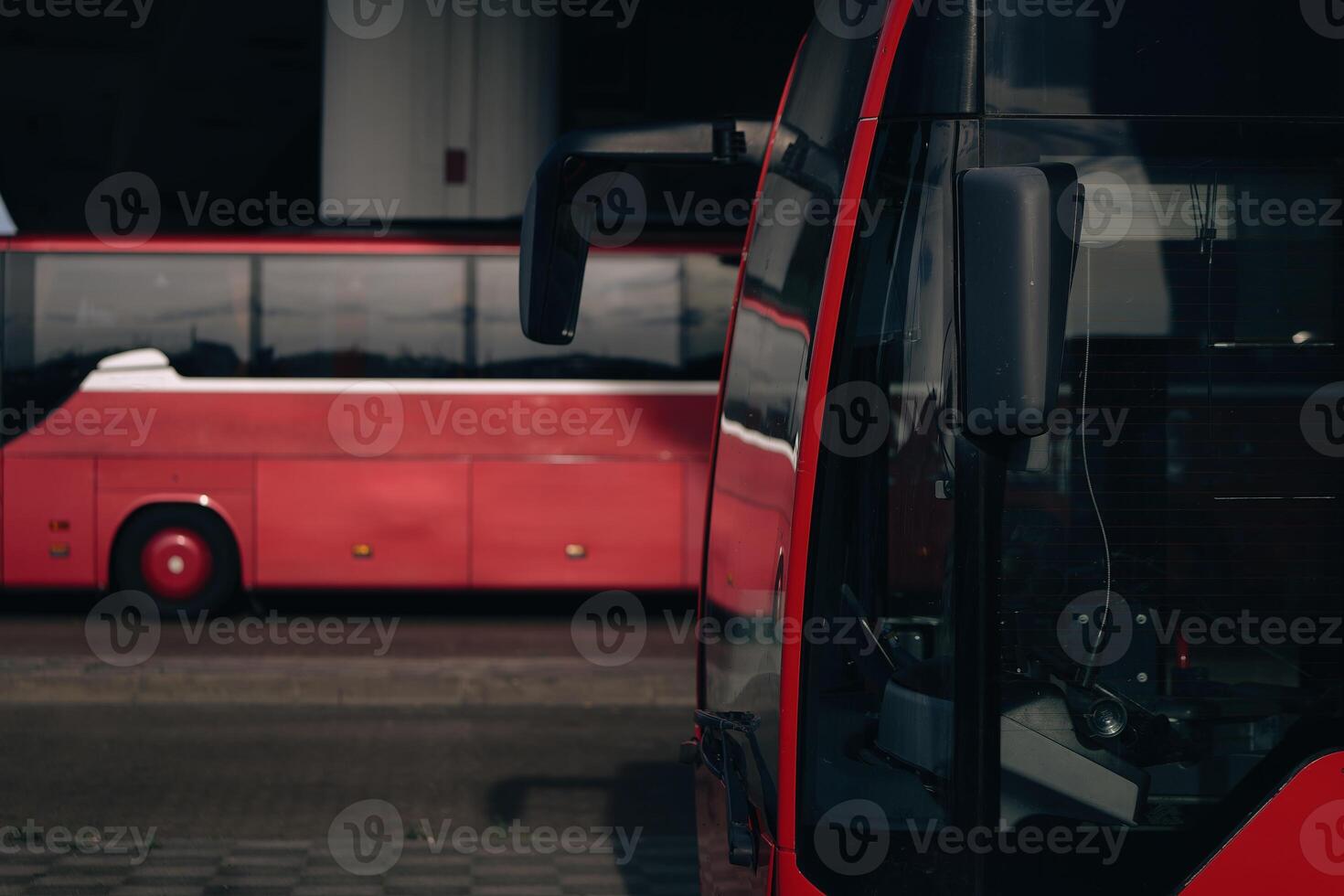 red bus with a black mirror is next to another red bus photo