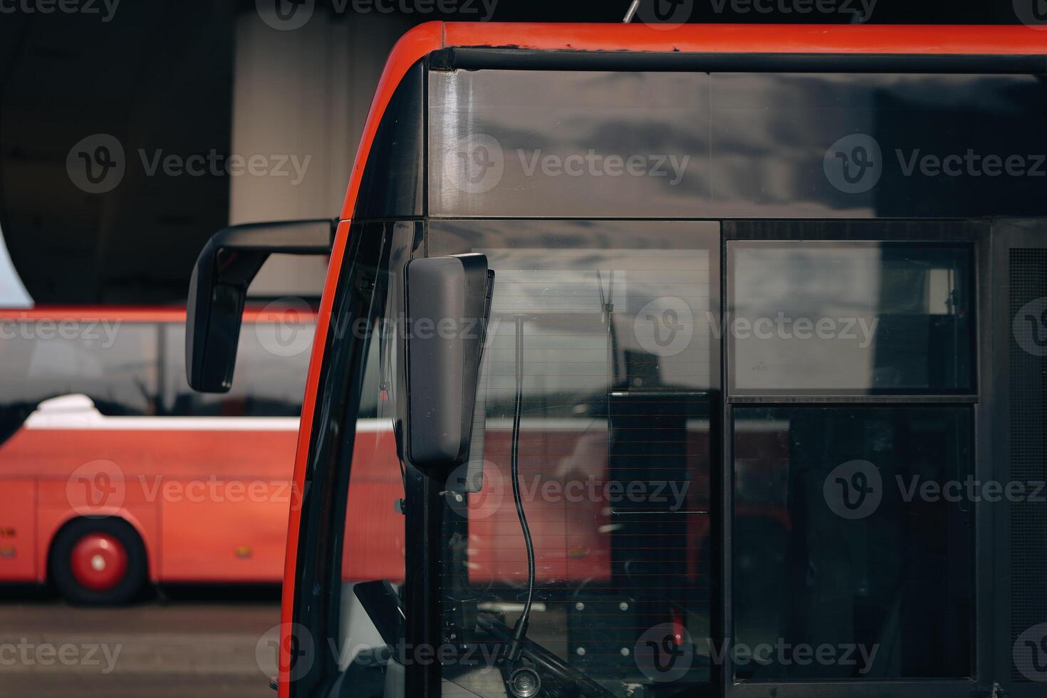 red bus with a black mirror is next to another red bus photo