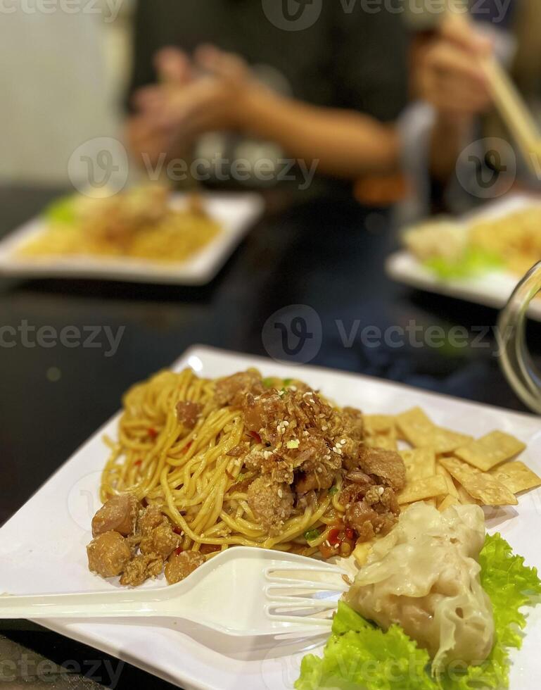 Indonesian food. noodles topped with chicken and dumplings. served on a square plate photo