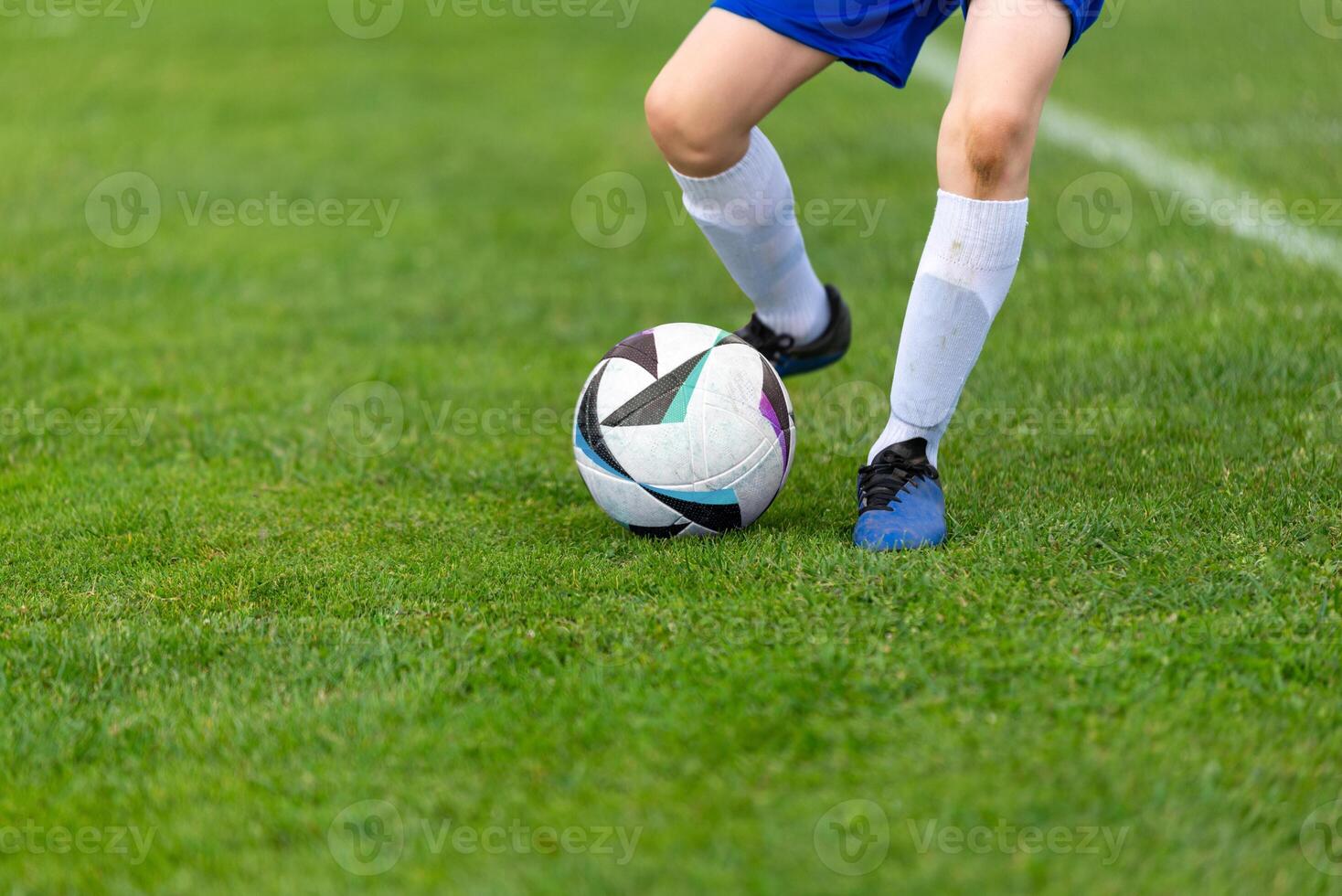 Young soccer player's kick ball. Ball and legs in sharp focus on a lush green field close-up photo
