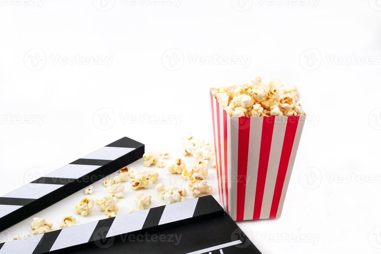 Focus of popcorn and blur clapperboard or movie slate black color on white background. Cinema industry, entertainment, production and film concept. photo