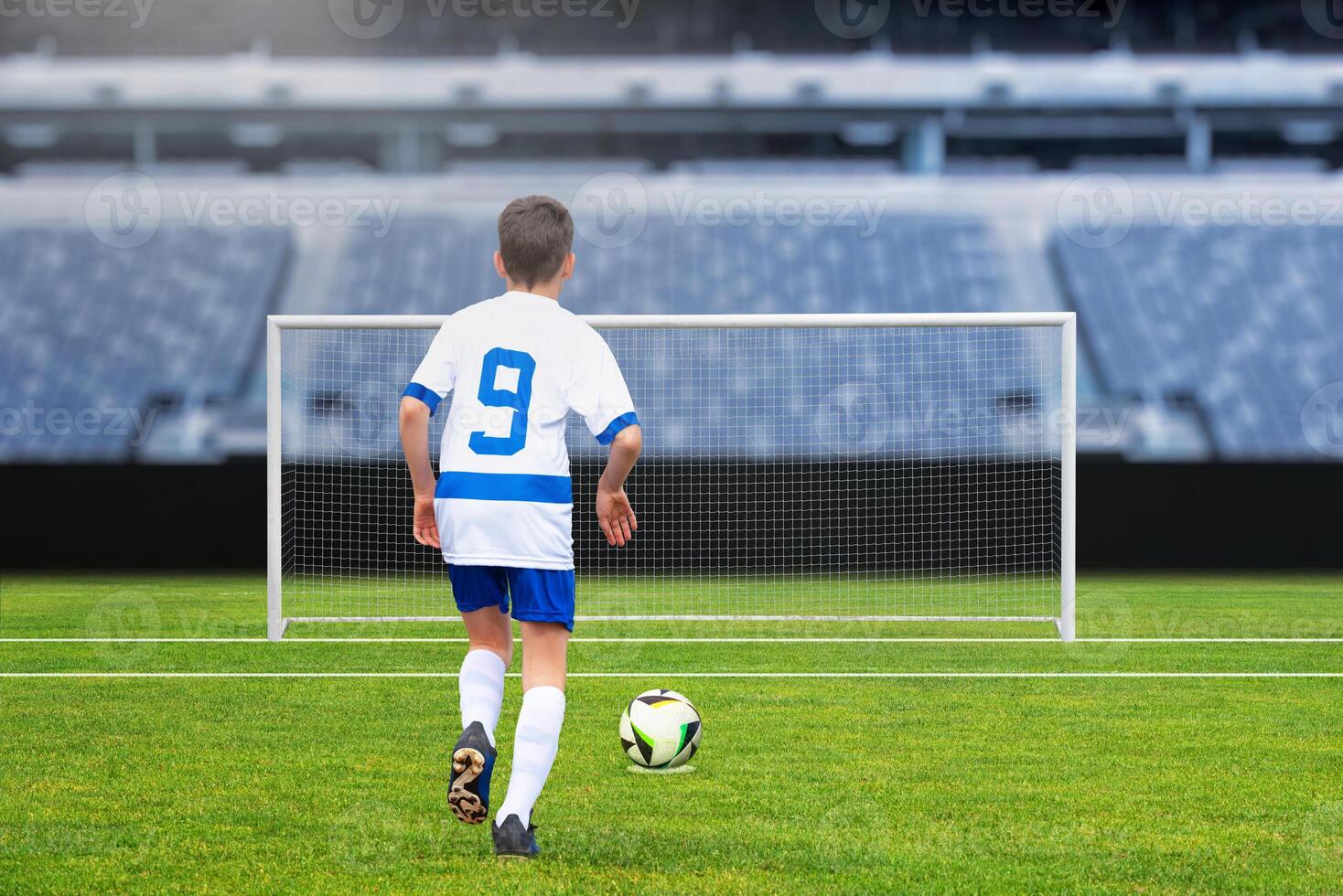 Young football player taking a penalty shot on an empty goal at a modern stadium, capturing the excitement of the game photo