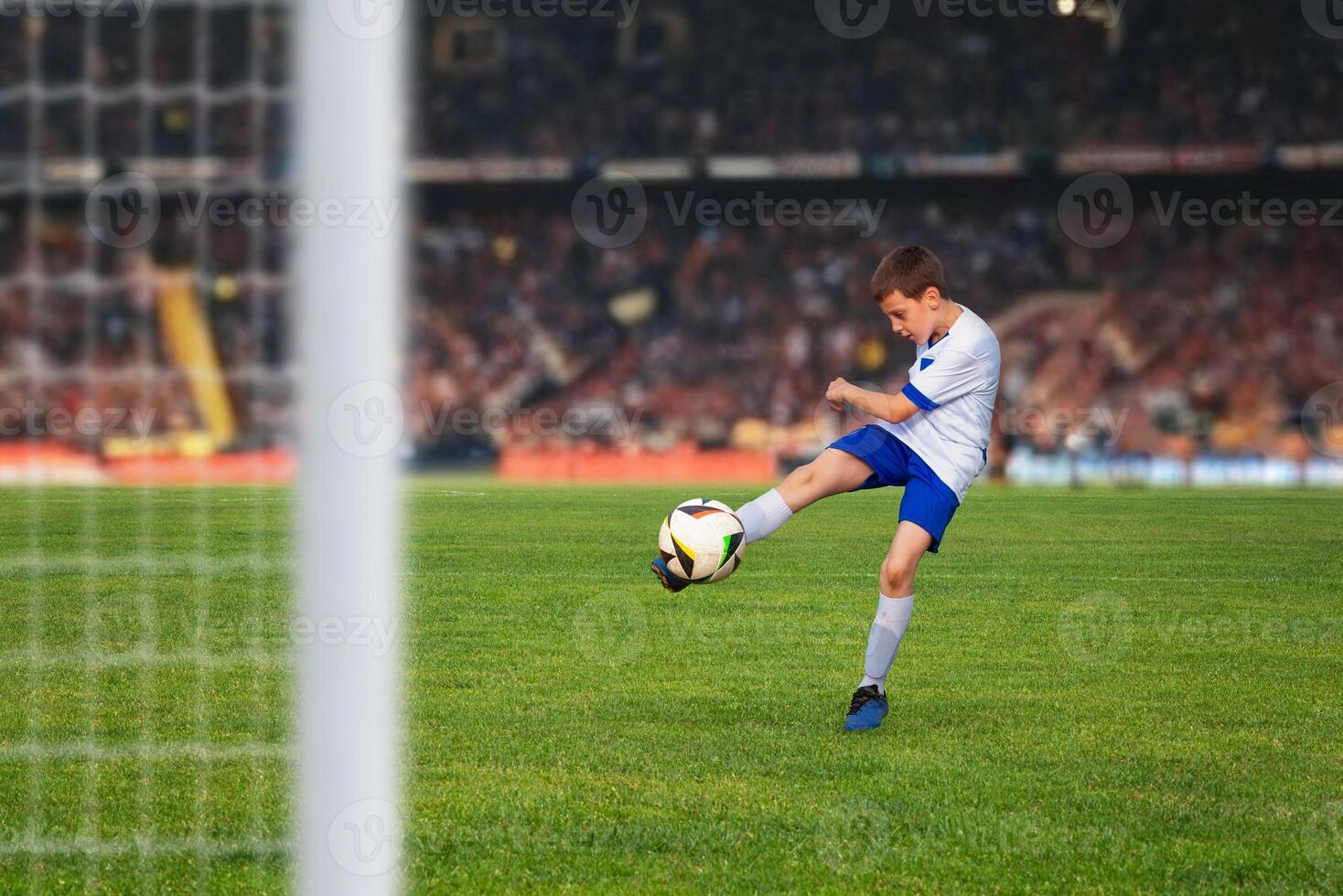 Young soccer player kicks the ball with determination, scoring a goal in a packed stadium under the bright lights of a thrilling match photo