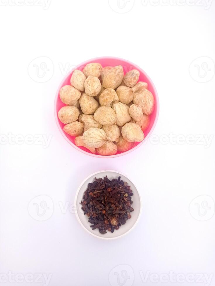 closeup of a bowl of Aleurites moluccanus in a pink plastic bowl and cloves in a small container isolated on a white background photo