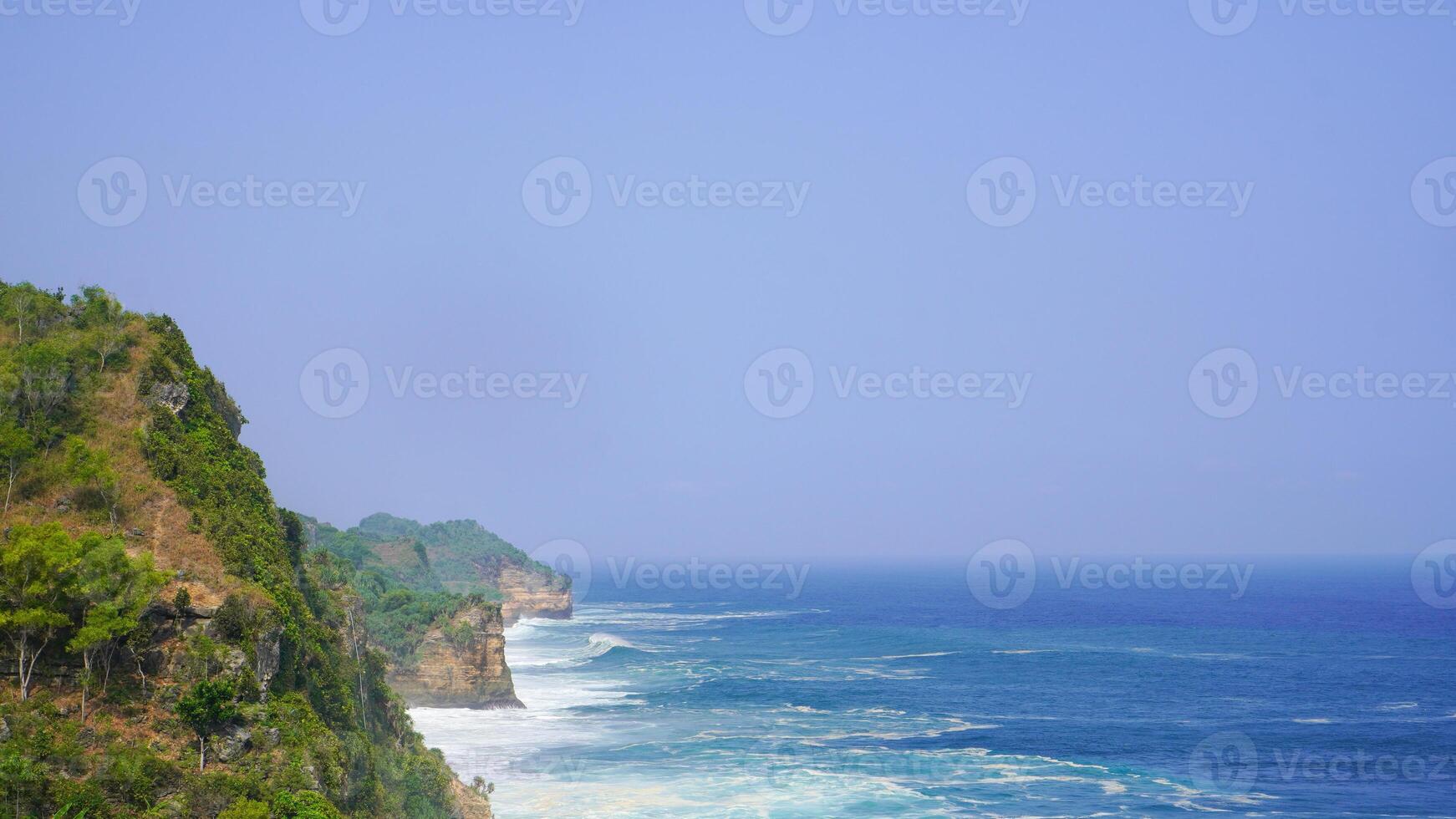 views of high cliffs on the shore, the beauty of the blue sea and dramatic rolling waves in the background. Seruni beach, Yogyakarta, Indonesia photo