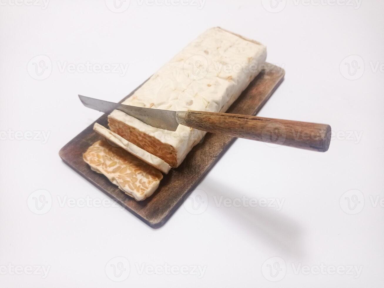 close up of raw tempeh on wooden cutting board and knife cutting tempeh isolated on white background. photo
