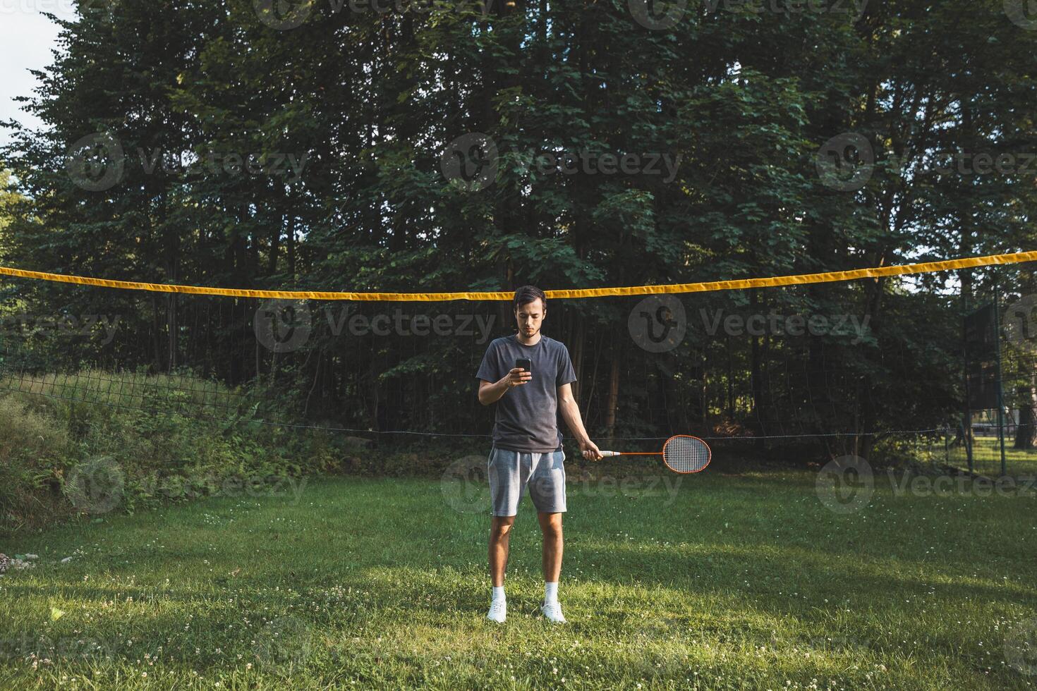 Addicted to the mobile phone even when playing badminton. A black-haired man holding a phone and playing sport. Modern combination of sport and technology. Problem of teenagers today photo