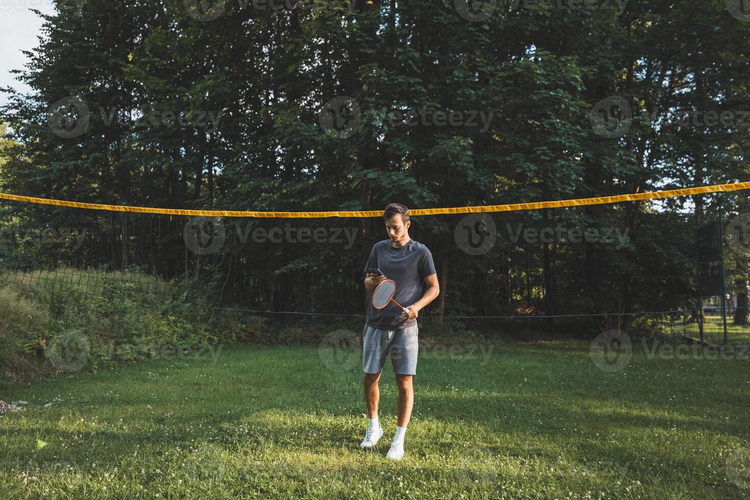 Addicted to the mobile phone even when playing badminton. A black-haired man holding a phone and playing sport. Modern combination of sport and technology. Problem of teenagers today photo