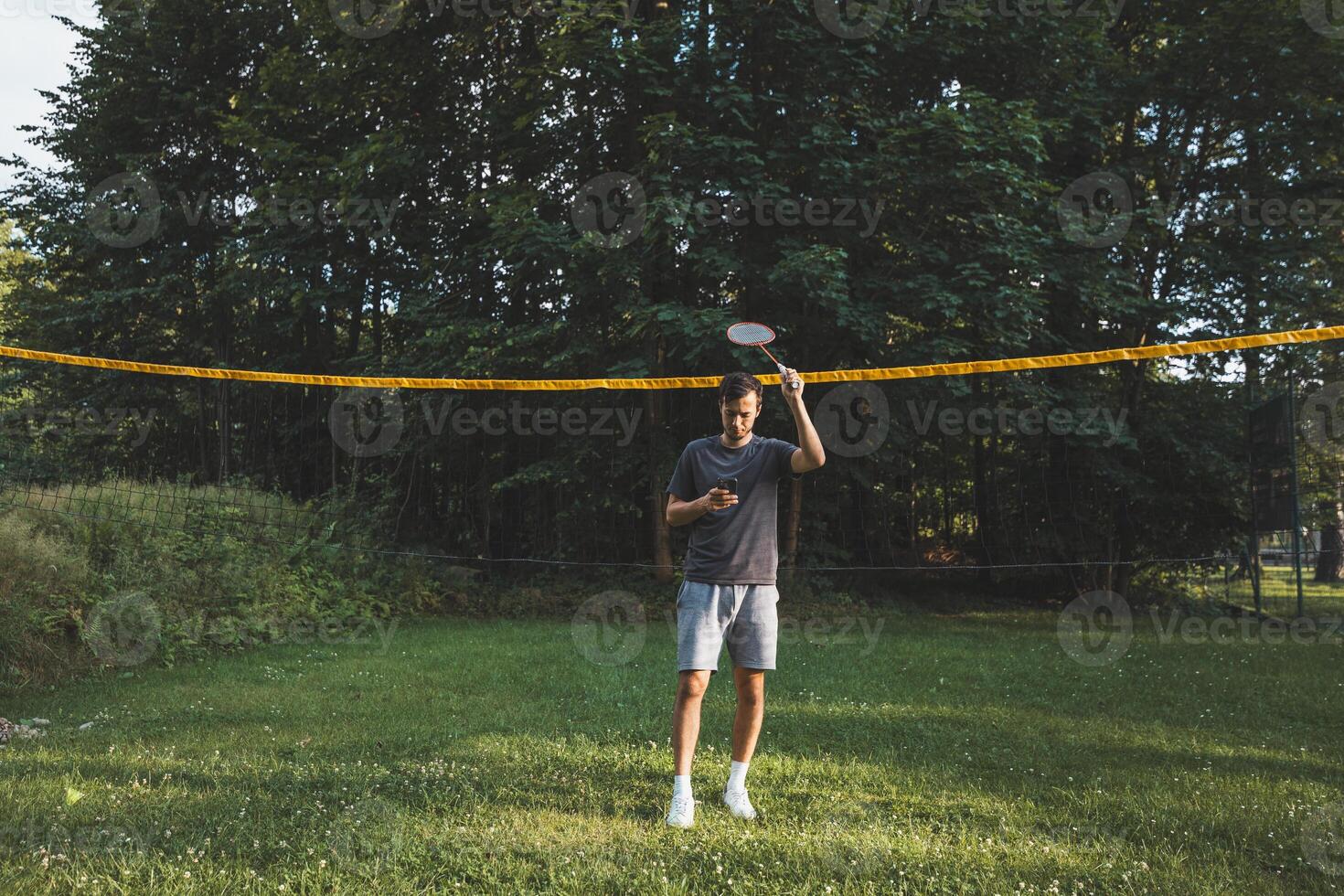 Addicted to the mobile phone even when playing badminton. A black-haired man holding a phone and playing sport. Modern combination of sport and technology. Problem of teenagers today photo