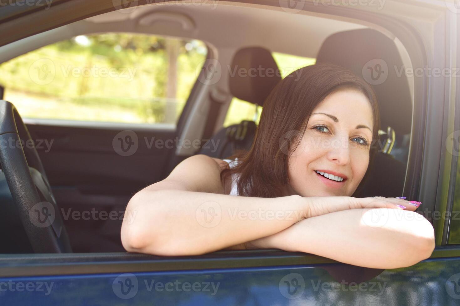 a portrait of a smiling woman sitting in the car, looking at the camera. photo
