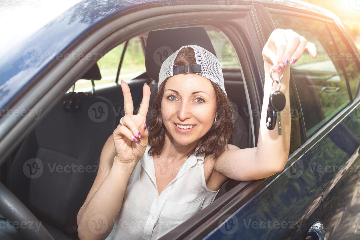 Beautiful woman in a hat holding keys to new bought car and smiling at camera in summer day photo