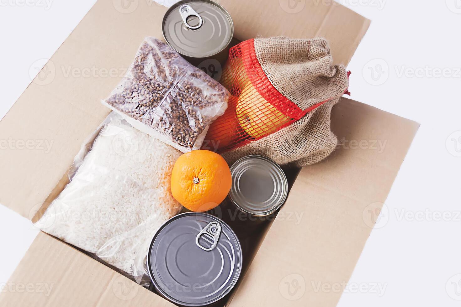 Canned food, fresh apple fruits, buckwheat and rice packs in a cardboard box. Food donation, delivery theme. photo