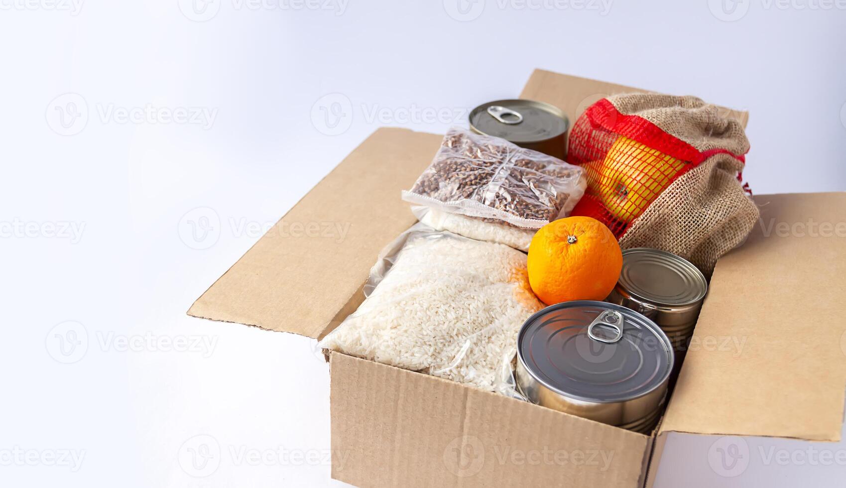 Canned food, fresh apple fruits, buckwheat and rice packs in a cardboard box. Food donation, delivery theme. photo