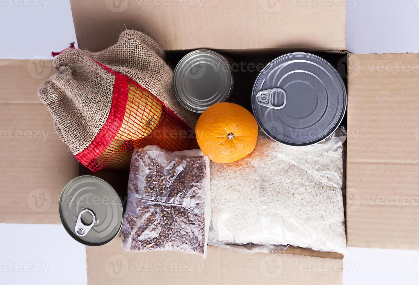 Canned food, fresh apple fruits, buckwheat and rice packs in a cardboard box. Food donation, delivery theme. photo