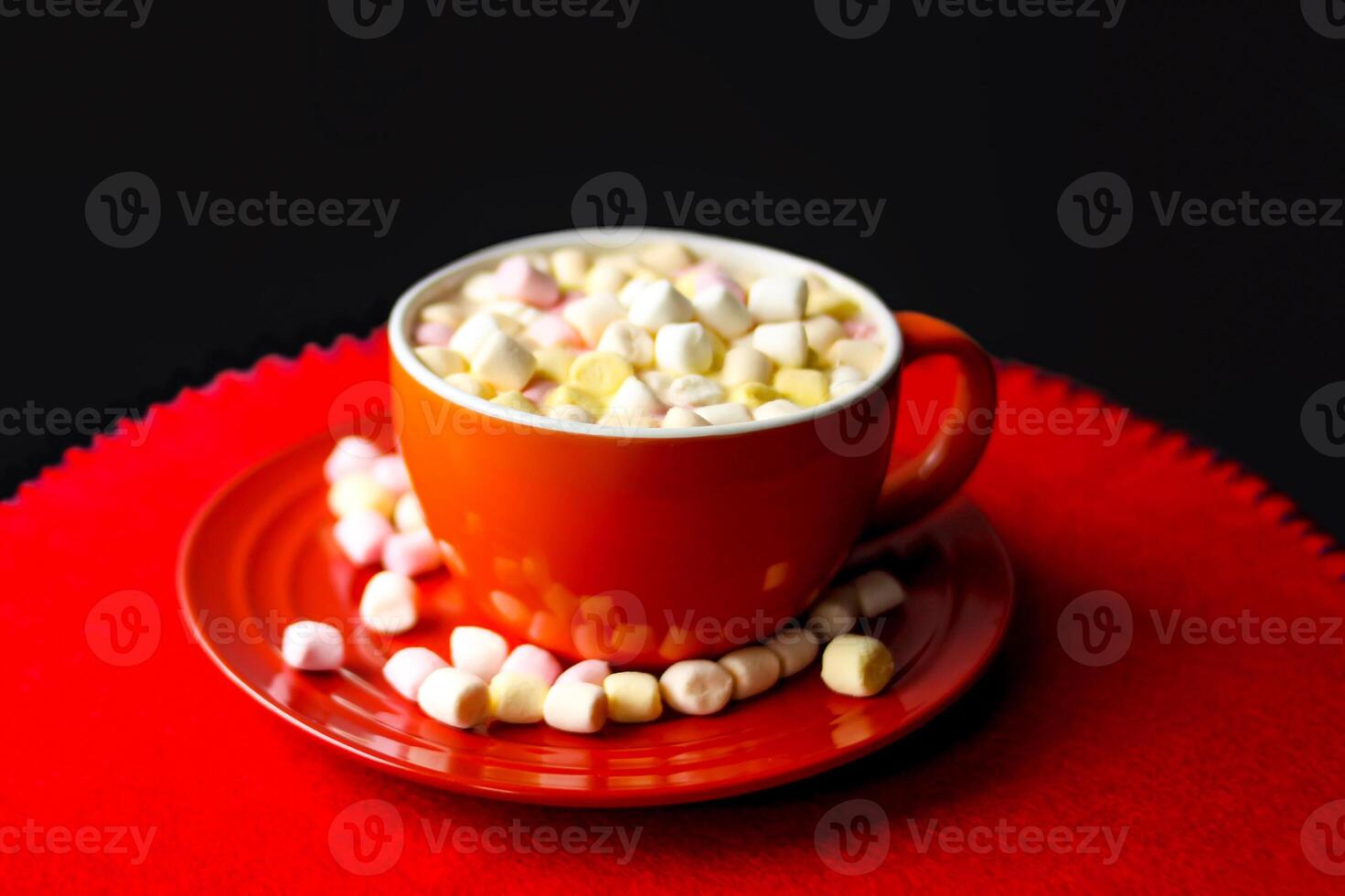 Cocoa drink with colorful small marshmallows on red background photo