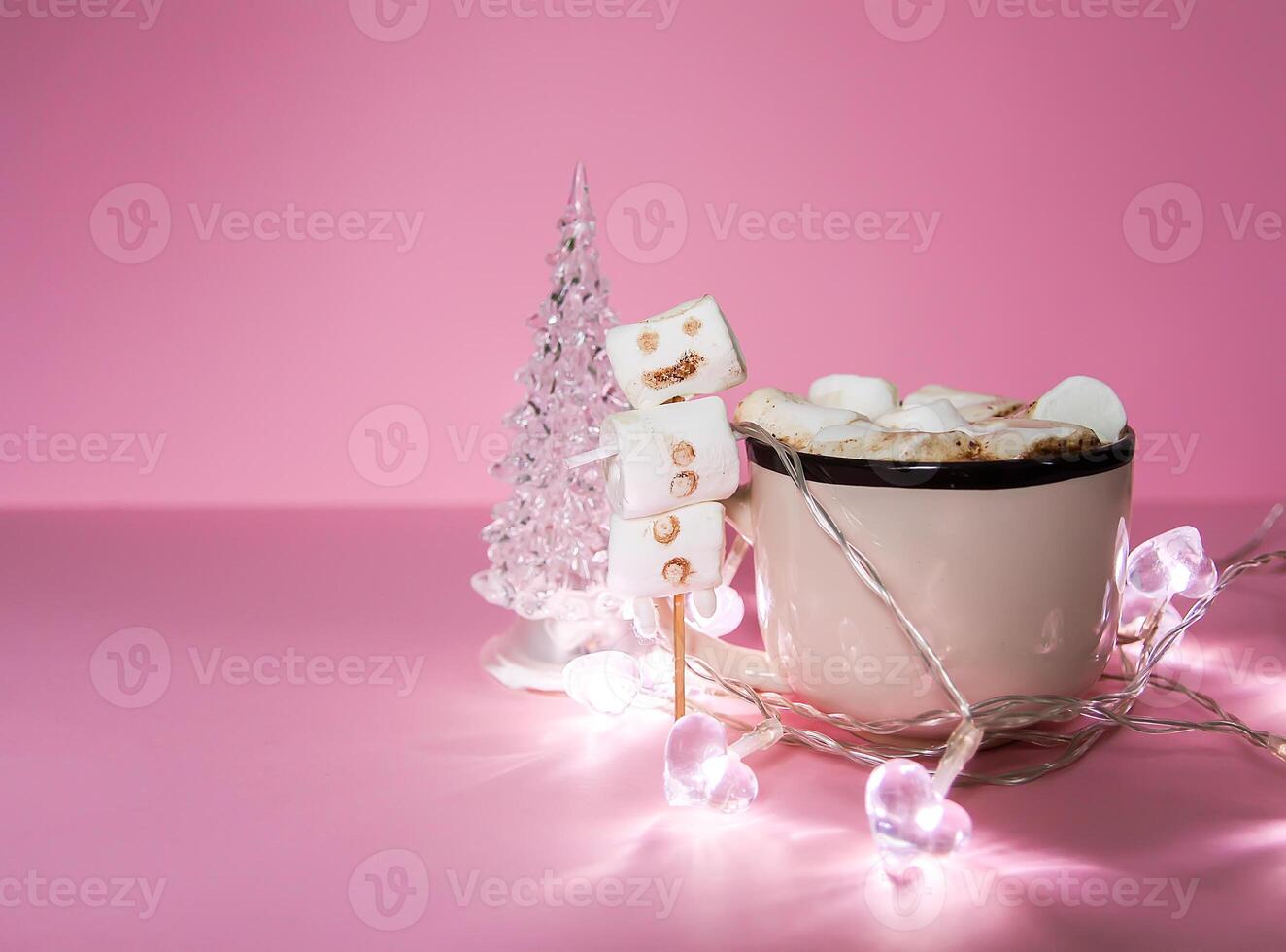 Ceramic mug with hot fresh cocoa drink and handmade funny marshmallow snowman on soft pink background. photo
