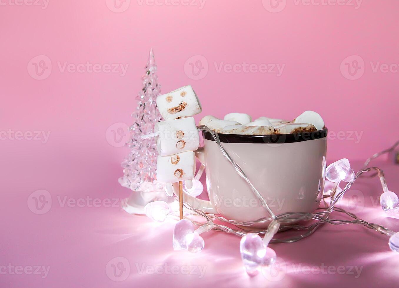 Ceramic mug with hot fresh cocoa drink and handmade funny marshmallow snowman on soft pink background. photo