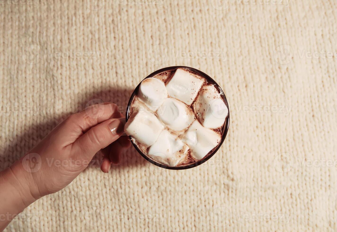 Woman's hand holding ceramic mug with hot fresh cocoa drink with marshmallows photo