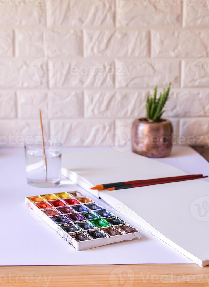 Watercolor paints, brushes, water in glass and paper on white background. Flat lay, top view photo