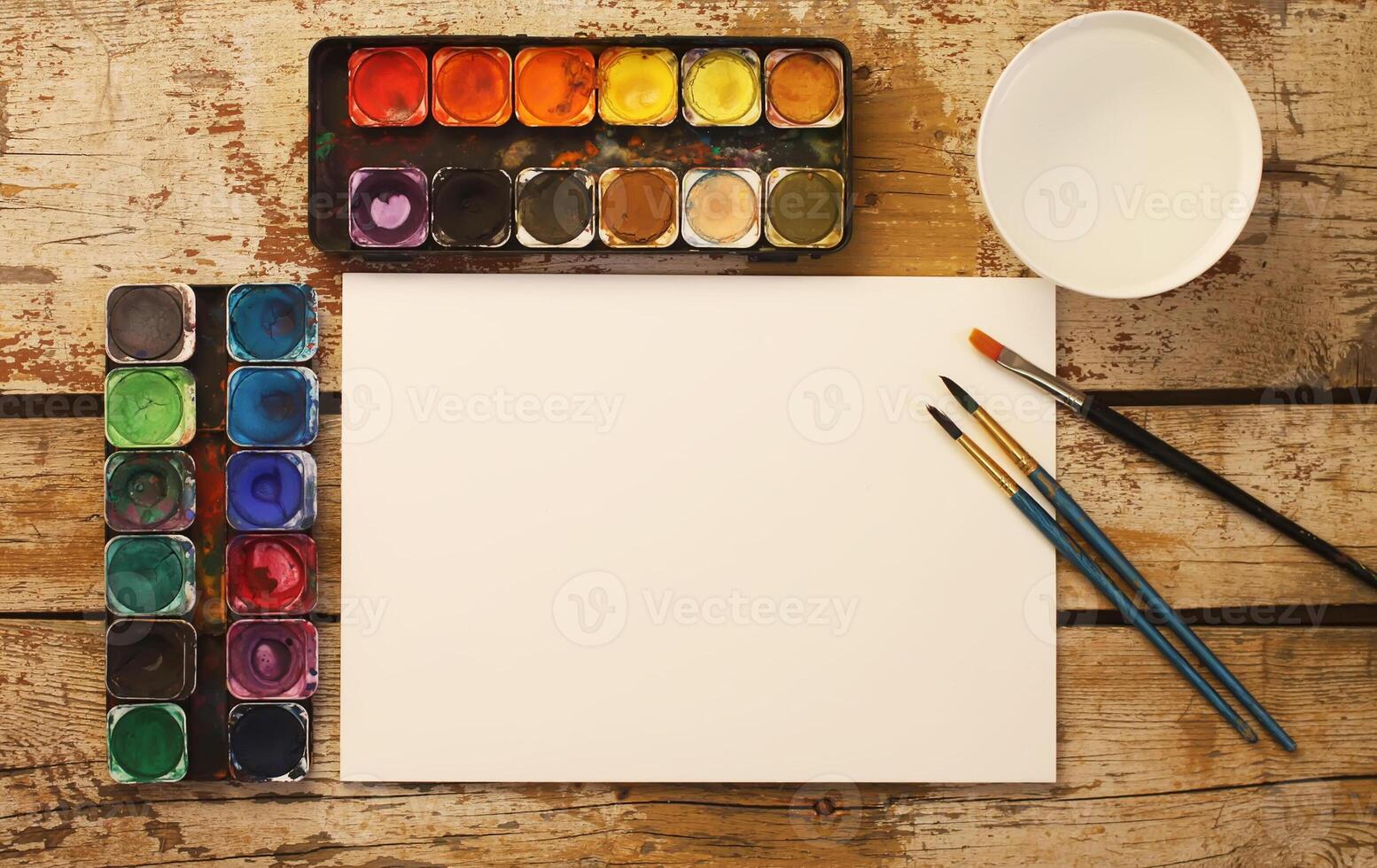 Paper, watercolors, paint brush and some art stuff on wooden table photo
