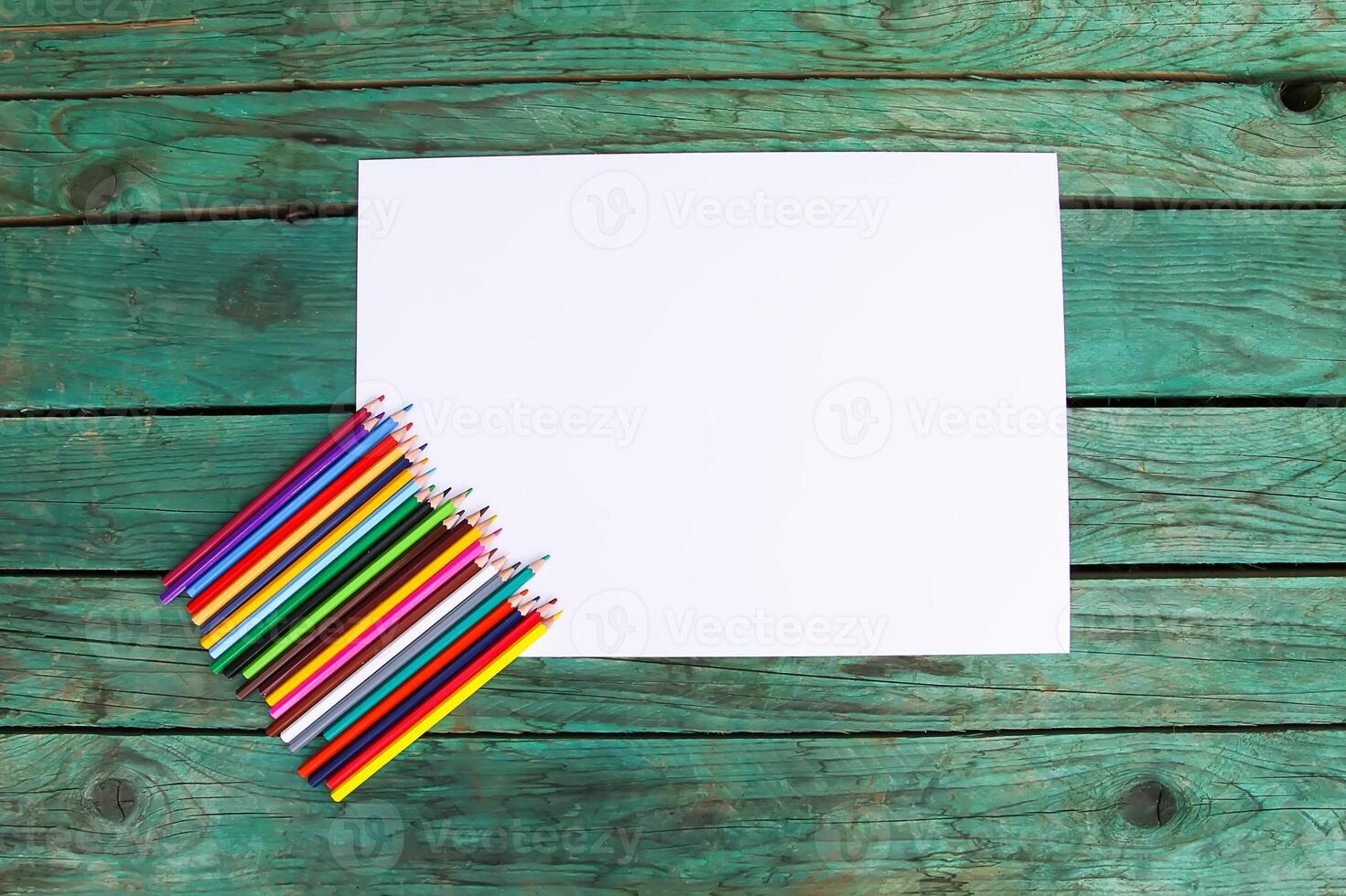 White paper sheet and colored pencils on wooden aged background. photo