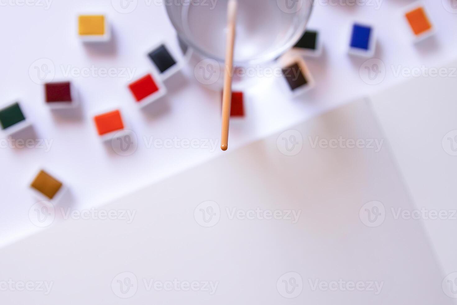 Watercolor paints, brush, water in glass and paper on white background. Flat lay, top view photo